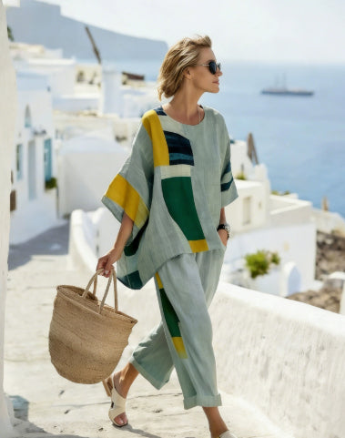 Woman in a colorful outfit walking on a sunlit street with white buildings and blue sky.