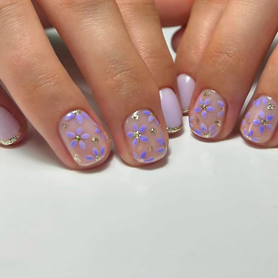 Close-up of hands with pink and purple floral nail design on a white background