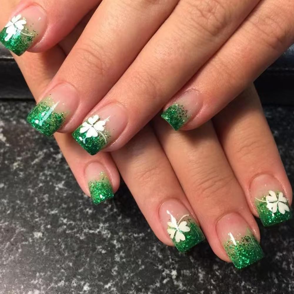 Nails with green glitter and white flower designs on a dark surface