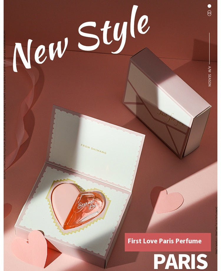 Heart-shaped perfume bottle in an open box with 'First Love Paris Perfume' branding on a red background.