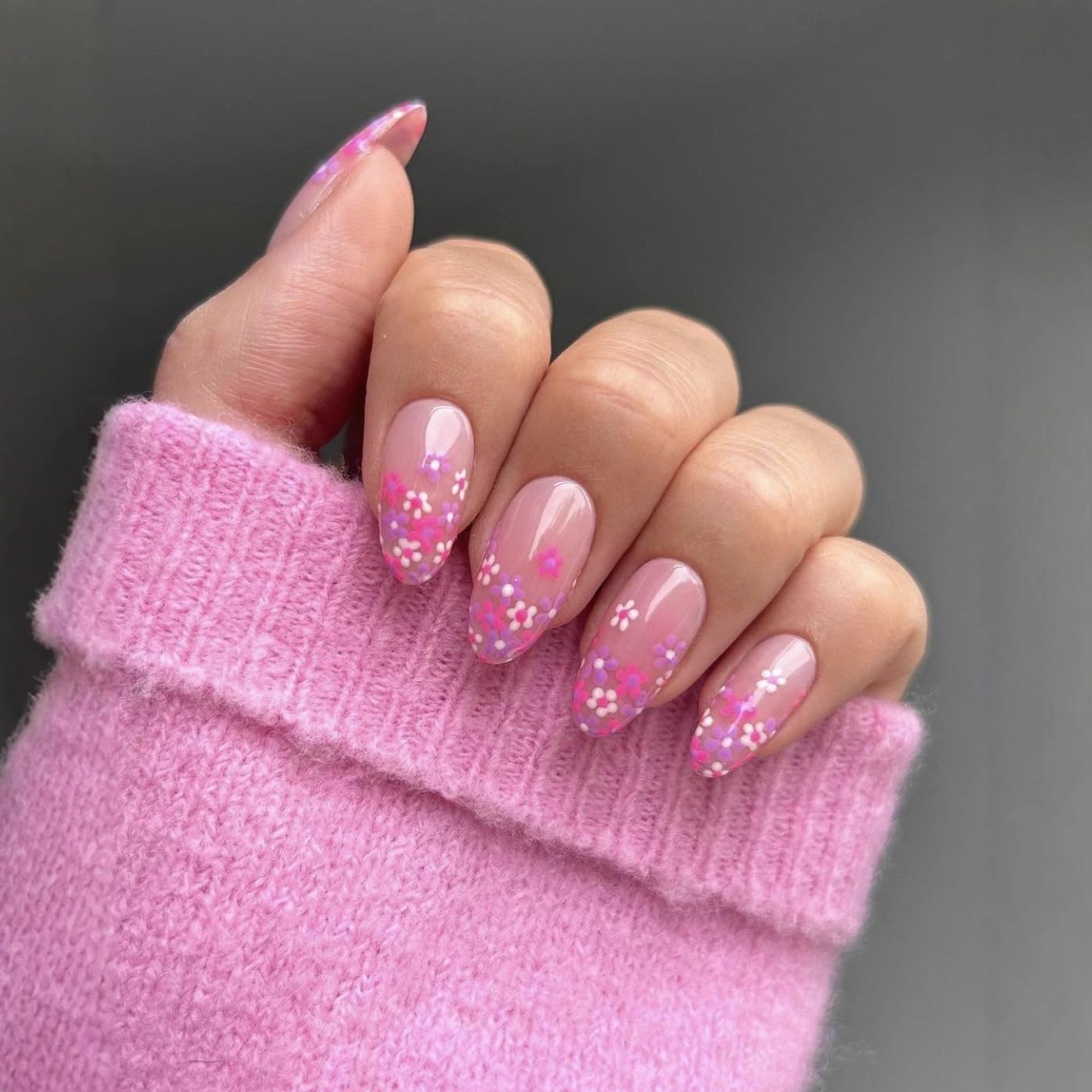 Hand with pink glittery nails wearing a pink sleeve against a dark background