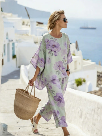 Woman in a floral outfit walking on a sunlit street with white buildings and blue sky.
