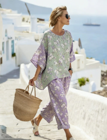Woman in a floral outfit walking on a sunlit street with white buildings and blue sky.